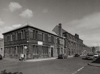 General view from SW of SW corner of works, showing elevations onto Norman Street (left) and French Street (right).  The view also shows the coloured enamel bricks decorating the office building occupying the SW corner of the works