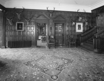 Interior. Ground floor view of entrance hall from East looking through to the sitting room and dining room beyond showing the panelled walls and pedimented doorcases