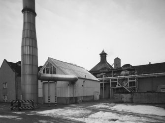 General view from SE of Still House, with Boiler House and flue (left) and Kiln in distance.