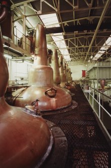 General view from ENE within Still House, showing row of 8 stills, all but 2 of which were built by A.Forsyth of Rothes. The stills, which are coal fired, are arranged with wash and spirit stills in pairs, the latter being the smaller stills (with the more rounded necks).