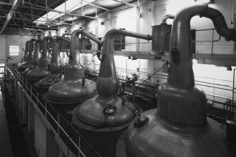 Elevated ground view from WNW within Still House, showing row of 8 stills, all but 2 of which were built by A.Forsyth of Rothes. The stills, which are coal fired, are arranged with wash and spirit stills in pairs, the latter being the smaller stills (with the more rounded necks).