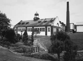 Exterior view from SW of former cooperage, also showing boilerhouse chimney, and examples of topiary typical of the distillery gardens
