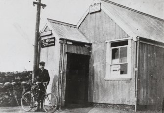 Achiltibuie, Post Office.
View of Post Office with man with bicycle in foreground.
