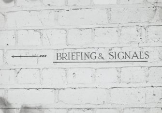 Tain Airfield Operations Block, upper main corridor, detail of sign painted on wall to ' Briefing & Signals'.