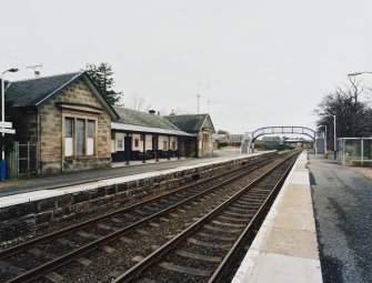View from E of NE side of station, with tracks and platforms in the foreground, and footbridge beyond