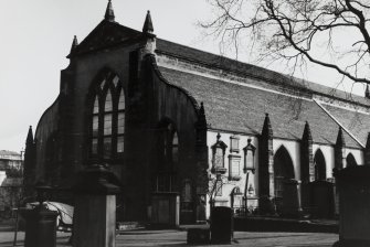 General view of harled West gable and South wall with part of churchyard in foreground.