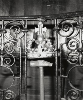Interior-detail of coronet in wrought iron balustrade in front of curved bench in chapel.