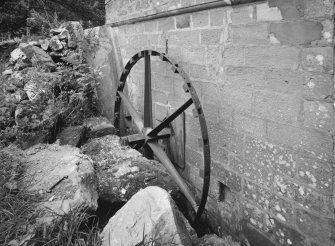 Detailed view of undershot start & awe water wheel situated on W gable of mill, comprising a single iron rim with six arms and 24 sockets for paddles (all missing).