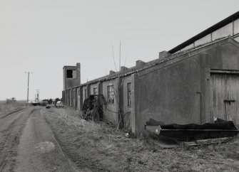 View N showing full length of a brick and concrete accommodation hut with tower for water tank.
