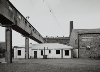 Newtongrange, Lady Victoria Colliery, Time Office and Lamp Station (Former Cement Store)
View from east of pit-head buildings, showing (left to right) overhead walkway, time office and lamp station (the former cement store) (centre), New Visitor Centre (formerly the New Power Station) (background), and the British Coal archive (formerly the colliery workshop) (right), with boilerhouse chimney in background