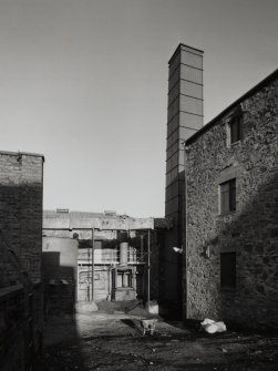 View from SW of rear of Still House, showing worm tub of No.1 Spirit Still (left) and condenser of Wash Still (right), and chimney stack (right), with overhead flue connecting it to neighbouring Boiler House.  Note that the chimney also serves a flue connecting it to the Wash Still (behind)