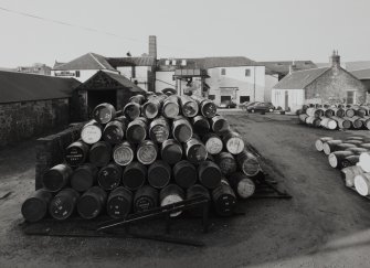 Elevated view from NE of main production block of distillery, including Still House, Mash House, Mill House and Tun Room, with yard (full of casks) in foreground, and Office (right))