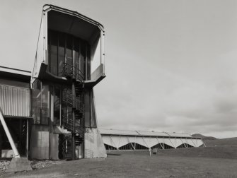 View from south of north east corner of factory, comprising two steel-framed blocks (completed in 1980), and the end of a raised walkway (left) with emergency external spiral stair.  The more distant block (right) was the receiving area.