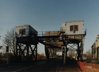 General view from E of E end of bridge, showing two towers supporting control cabins (with connecting overhead gantry) and in centre, rolling/lifting span
