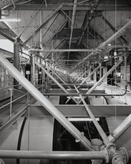 Drum Room:  general interior view E down centre of Drum Room, showing conical bases of 24 steeps above, and 24 rotating maltings drums (with rim gears) below.  Also visible at this level are electrical control panels on either side