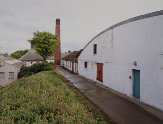 View from WNW of block containing duty-free warehouses and filling store, with boiler-house chimney stack in background.