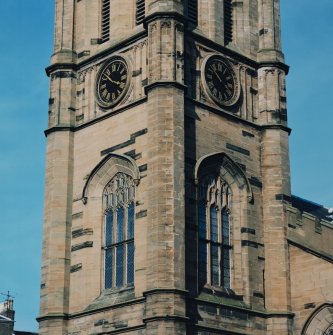 View of second stage of tower showing traceried windows and clock faces.