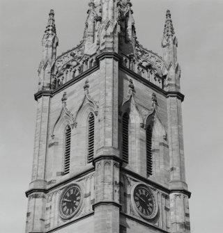 View of top stage of tower showing belfry openings above clock faces, wallhead parapet and pinnacles.