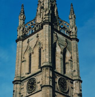 View of top stage of tower showing belfry openings above clock faces, wallhead parapet and pinnacles.