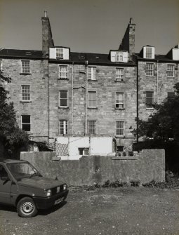 View of the rear of the building with an additional building in the stages of being demolished in the foreground, seen from the West.