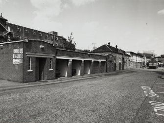 View of south east of range of buildings at west side of works, containing garages, electrical switchroom, electricians' workshop and store, canteen (upper floor), plumbers' shop, paint shop and in the distance, tanks of the Carbon Dioxide Plant.