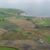 General oblique aerial view looking across the cropmarks of the barrows, pits, field boundaries and enclosure at West Myroch towards Port Logan, taken from the NE.