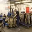Interior.  Cask Rebuild Process. Jamie O' Hare, a cooper for 41 years, building or 'rising' a cask. The cask is being tightened with the windlass to allow the cooper to hammer on the other end or chime hoop. This tightens up the cask shell. To his right, note the removed red coded riser end or chime hoop which has been removed. the tightening up of the cask when it was turned loosend the temporary end hoop, so a smaller end hoop is hammered on by the cooper. Both of the end hoops will be replaced again after the Chappinng Out phase of the process.