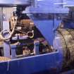 Interior.  Cask Rebuild Process. Croze Machine. A chapped out cask shell with its four temporary truss hoops being held by its ends. The cooper closes the door of the booth and switches on the machine which cuts the chime and groove of the cask.