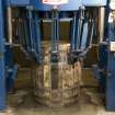 Interior view of Cask Rebuilding and Rejuvination Process, Dundashill Cooperage, Glasgow. Vertical Cask Hoop Driving Machine. Second Cask Hoop Drive. The cask sits vertically in the machine. The arms of the machine are in the process of forcing one of the bilge hoops down for a second time after the cask has cooled down after steaming or charring. This tightens the cask by forcing the oak staves and chimes together. The cask is now ready for testing.
