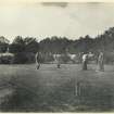 View of garden buildings and croquet lawn with group of people playing croquet, probably at Inchrye Abbey.

