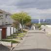 Street view showing partly terraced housing at Brick Row and Brewlands Avenue, Bo'ness, taken from the East. Each house is set back from the one before as they recede down the hill, and each has its own garage and direct access from the street. Grangemouth can be seen in the distance to the centre of the image. This photograph was taken as part of the Bo'ness Urban Survey to illustrate the character of the Hillcrest and Brewlands Area of Townscape Character.