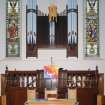 View of chancel area, showing communion table, pulpit, organ pipes and flanking stained glass windows.