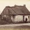 View of thatched house in Fenwick village with man at entrance.