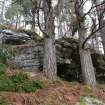 A rock shelter built into a rock outcrop with south east facing aspect; a plaster angel figure sits on a ledge above it, Inchnacardoch Forest Block, South Loch Ness