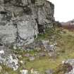 General view of the remains of a hut and two pens, set against the cliff.