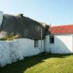 Side view of  19th century cottage with 'thatched piended roof' showing some grassy vegetation growth; Tiree, Balevullin.