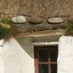 Detail of restored 19th century thatched cottage showing thatching, stone weights and wooden boarding above window; Tiree, Balevullin