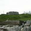Distant view of previously thatched 19th century stone cottage, only roof framework remaining; Ardheisker, North Uist.