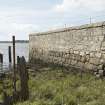 Walling on west side of estuary and remains of timber wharf posts, view from north east. Note the lower, darker-coloured stone courses of the original quay wall.