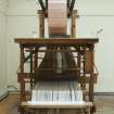 Interior. General view. Jaquard loom in gallery area. The warp beam is clearly visible as is the jacquard device above the loom. The holes and blanks on the cards allow the hooks in the frame to select or not select threads to create the complex patterns in the cloth