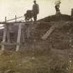 Excavation photograph of man with wheelbarrow on elevated walkway at Hillhead Broch. 