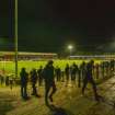 General view of the football pitch and stadium taken from the north east. Under floodlights.