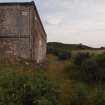 Explosives Magazine R35: view of the NW corner showing a characteristic concrete tub formerly associated with a downpipe and the WSW façade adjacent to the metalling marking the course of the narrow gauge railway line (right)