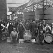 Laphroaig Distillery.
View of workers group, including Mrs Wishant-Campbell, alias Miss B. Williamson, far right. Also including range of worm-tubs in background, demolished c.1960.