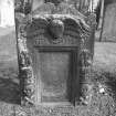 View from W of gravestone commemorating Thomas Angus and Jean White, d.1720; sunken inscription panel flanked by emblems of mortality, winged cherub at top with 'MEMENTO MORI' inscription beneath.