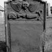 Gravestone commemorating Isobel McLunie, d.1769. Winged cherub; skull in profile, coffin, winged hourglass, crossbones.
