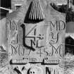 Perth, Greyfriars Burial Ground.
View of the gravestone of Alexander Bissett, 1777. A curved topped stone with palm fronds around a bundle of skeins of wool (?), and a central '4M' merchant's sign. The sheild is surrounded by initial: 'I.Y, M.D, J. Y, M.M, 1745'. Under the initials is a Memento Mori ribbon, further initials and dates ('I.S, 1765, E.C') and crossed bones, a skull and an hourglass.