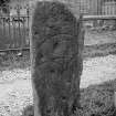 Pictish symbol stone standing in kirkyard. View of reverse, showing three circles, crescent and V-rod, and cup-marks.
Half-plate glass negative.