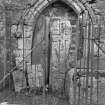 View of sculptured stones and arched doorway in railed enclosure.
Original negative captioned: 'Sculptured Cross Stones, Old Church of Tullich near Ballater July 1902'.