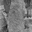 View of Pictish symbol stone standing beside railed burial enclosure in kirkyard.
